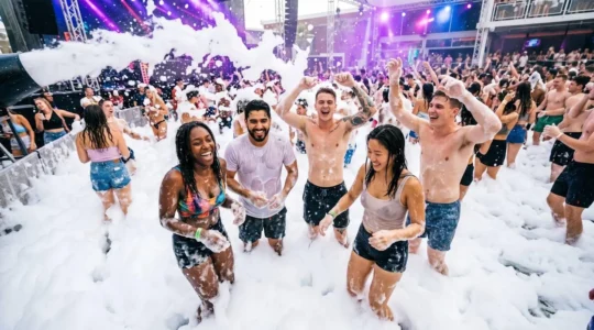 Junge Leute tanzen lachend in einer großen Schaumwolke bei der Schaumparty in Lloret de Mar.